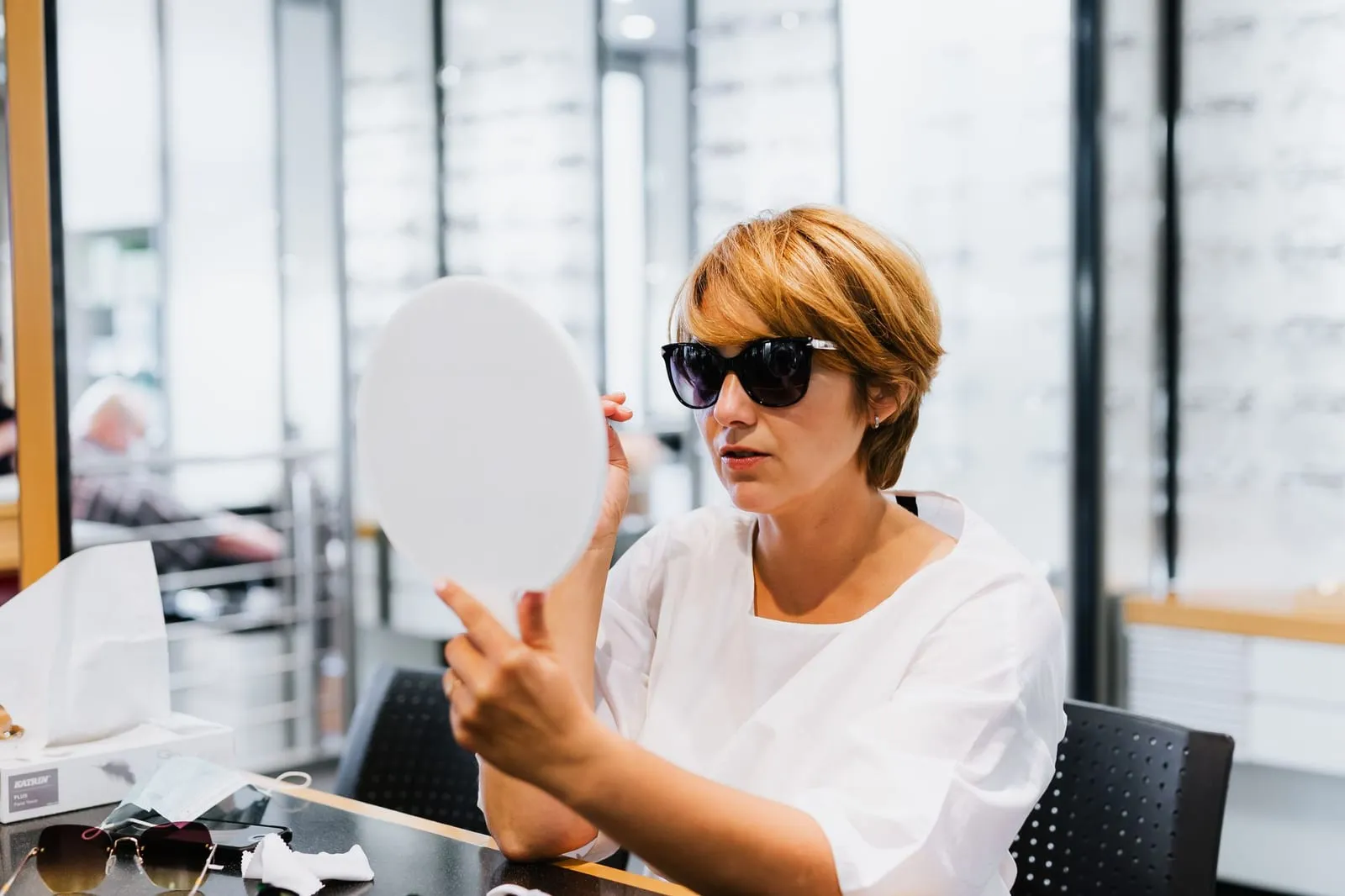 Doamnă care probează ochelari de soare în oglinda unei optici